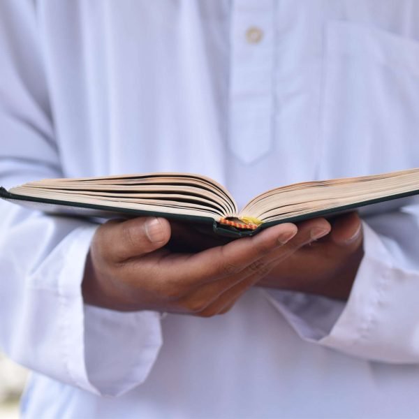 Holy Quran in hand with arabic calligraphy meaning of Al Quran. Islamic concept background